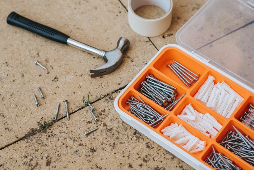 Overhead view of a toolkit with a hammer, screws, and anchors on a concrete surface.