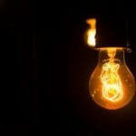 Close-up view of an illuminated vintage light bulb with glowing filament against a dark background.